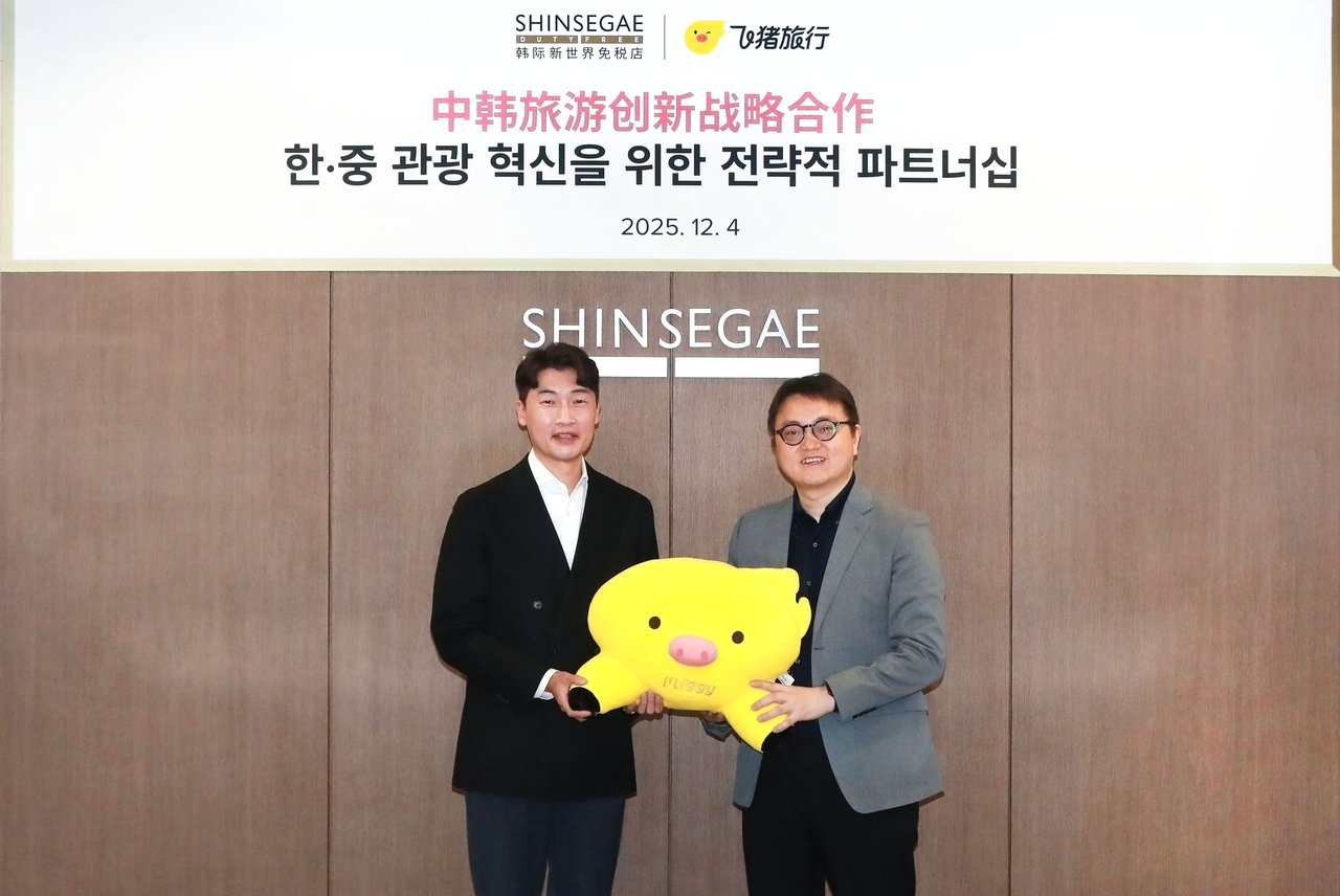 Shinsegae Duty Free Senior Vice President Kim Hyun-chul (left) and Fliggy Global General Manager Zhou Xiaochen pose with Fliggy’s flying-pig mascot after signing a memorandum of understanding at Shinsegae Duty Free’s Seoul headquarters on Thursday. (Shinsegae Duty Free)