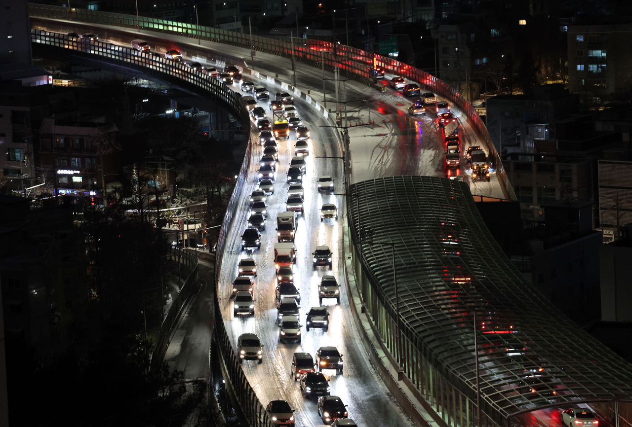 Vehicles are moving slowly on snow-covered roads along the road in Hongje-dong, Seodaemun District, Seoul, Thursday. (Yonhap)