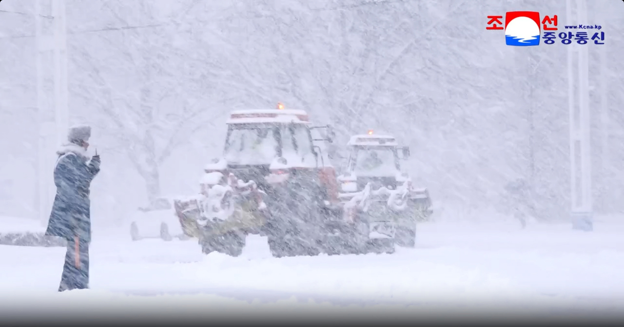 A pedestrian walks by while a snowplow clears snow from a road in Pyongyang on Thursday. (KCNA via Yonhap)
