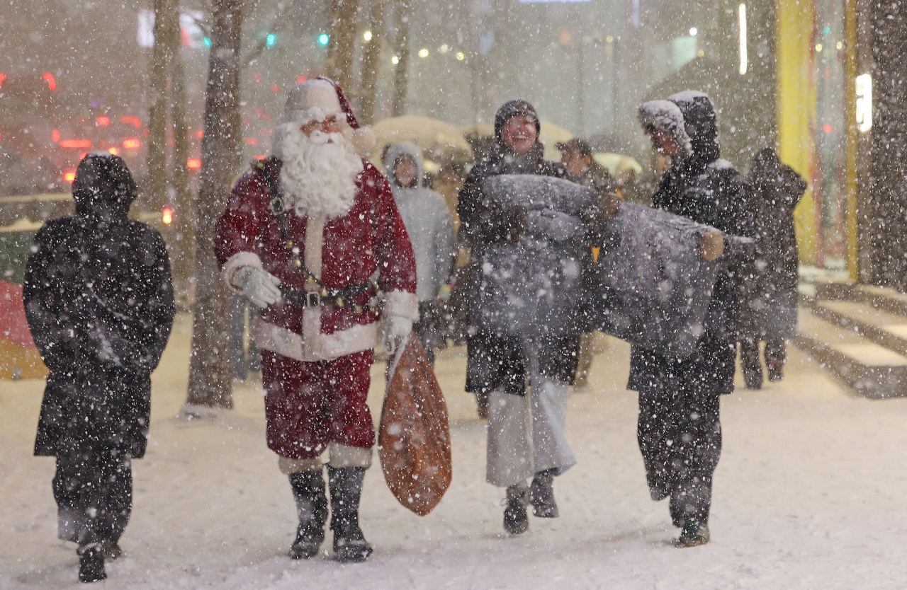 A Santa and other pedestrians walk through the season’s first major snowfall near Hongdae, in Seoul, Thursday.  (Yonhap)