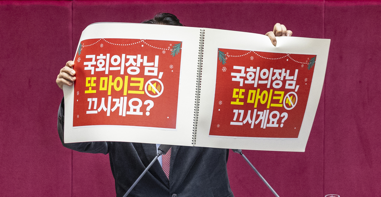 Rep. Kwak Kyu-taek of the People Power Party holds a placard reading, “Mr. Speaker, will you turn off the mic again?” during a filibuster at a plenary session of the National Assembly on Thursday. (Yonhap)