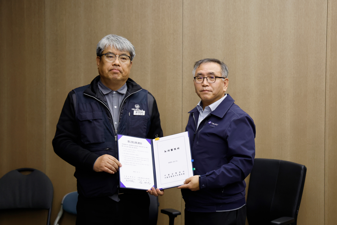 Seoul Metro’s acting head Han Young-hee (right) and Kim Tae-gyun, chair of the Seoul Transit Corporation Labor Union, hold the signed collective bargaining agreement after reaching a deal on Friday in Seoul. (Yonhap)