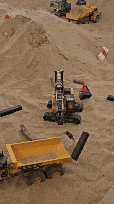 A remote-controlled crane lifts a plastic rod resembling rebar onto a dump truck in a large sandbox at Diggerz. (Choi Jae-hee/The Korea Herald)