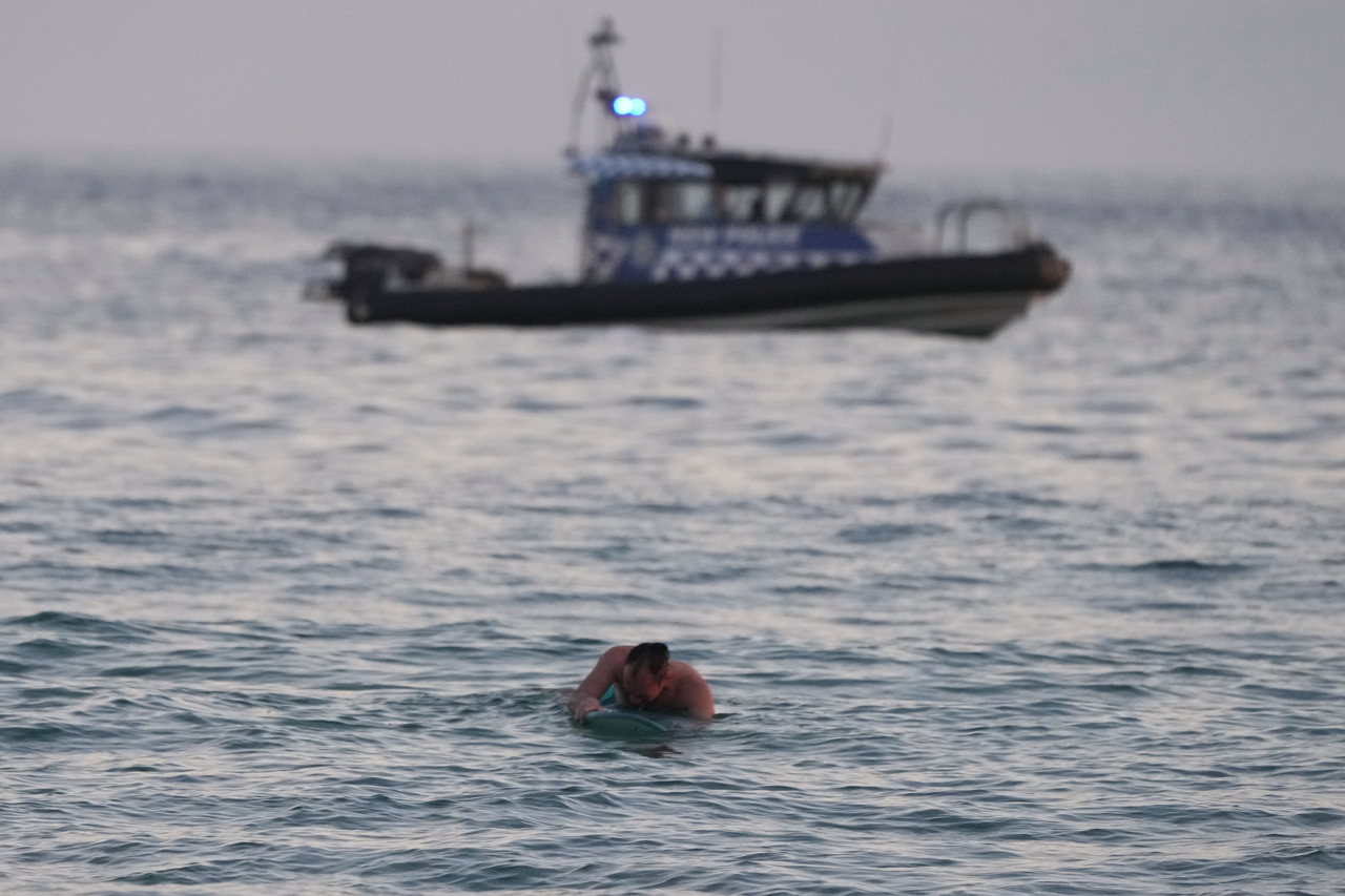 A surfer paddles back to shore as a police boat patrols the water after a reported shooting at Bondi Beach in Sydney, Sunday. (AP-Yonhap)