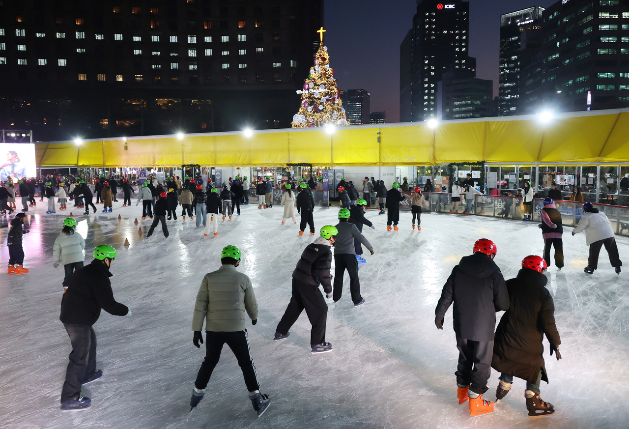 Skaters in green and red helmets enjoy the ice at Seoul Plaza on Friday. (Yonhap)