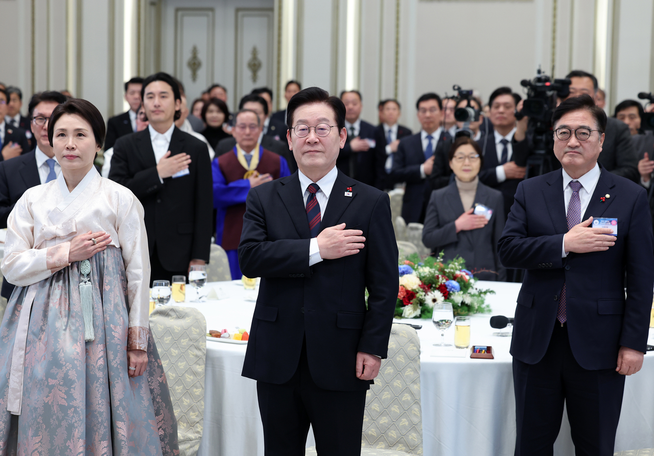 From left, front row: First lady Kim Hea Kyung, President Lee Jae Myung and National Assembly Speaker Rep. Woo Won-shik salute to the national flag at the president's New Year greetings in Cheong Wa Dae presidential compound on Friday. (Yonhap)