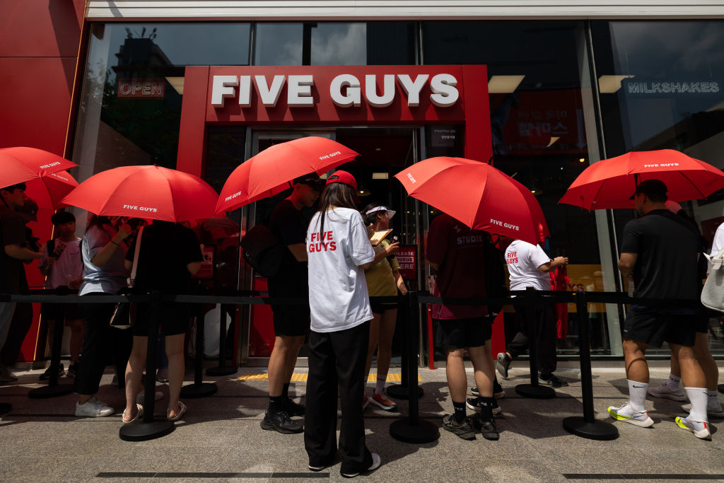 Customers hold umbrellas while waiting in line to enter the first Korean outlet of US burger restaurant chain Five Guys in Gangnam-gu, Seoul, on July 1, 2023. (Getty Images)