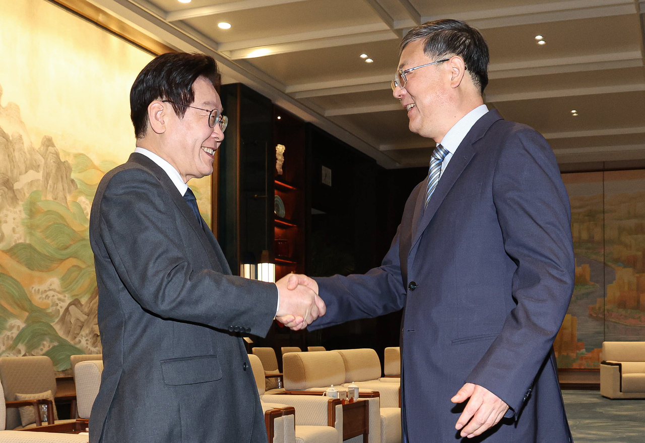 President Lee Jae Myung and Chen Jining, Shanghai’s Communist Party secretary, shake hands ahead of a dinner at the Shanghai World Expo Center on Tuesday. (Yonhap)