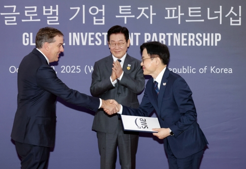 President Lee Jae Myung (C) claps his hands as Amazon Web Services Chief Executive Officer Matt Garman (L) hands an investment filing to Industry Minister Kim Jung-kwan during the Asia-Pacific Economic Cooperation gathering in the southeastern city of Gyeongju on Oct. 29, 2025. (Yonhap)
