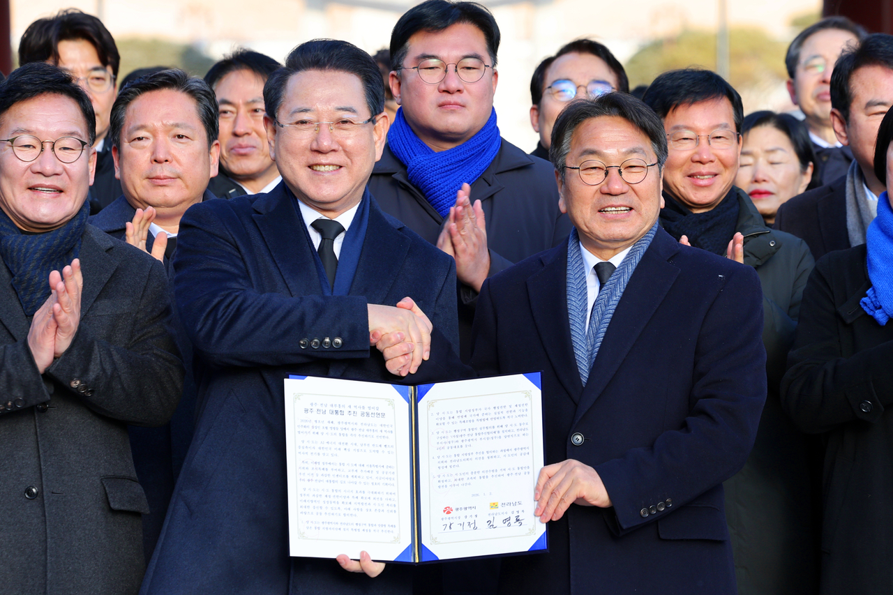 Gwangju Mayor Kang Gi-jung (center right) and South Jeolla Province Governor Kim Yeong-rok (center left) shake hands while holding a partnership certificate for the integration of the two municipalities during their visit to the Gwangju May 18 National Cemetery on Friday. (Yonhap)