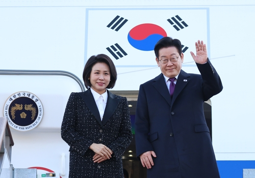 President Lee Jae Myung (R) waves as he and first lady Kim Hea Kyung prepare to board the presidential jet bound for Japan on Tuesday, at Seoul Airport in Seongnam, south of Seoul. (Yonhap)