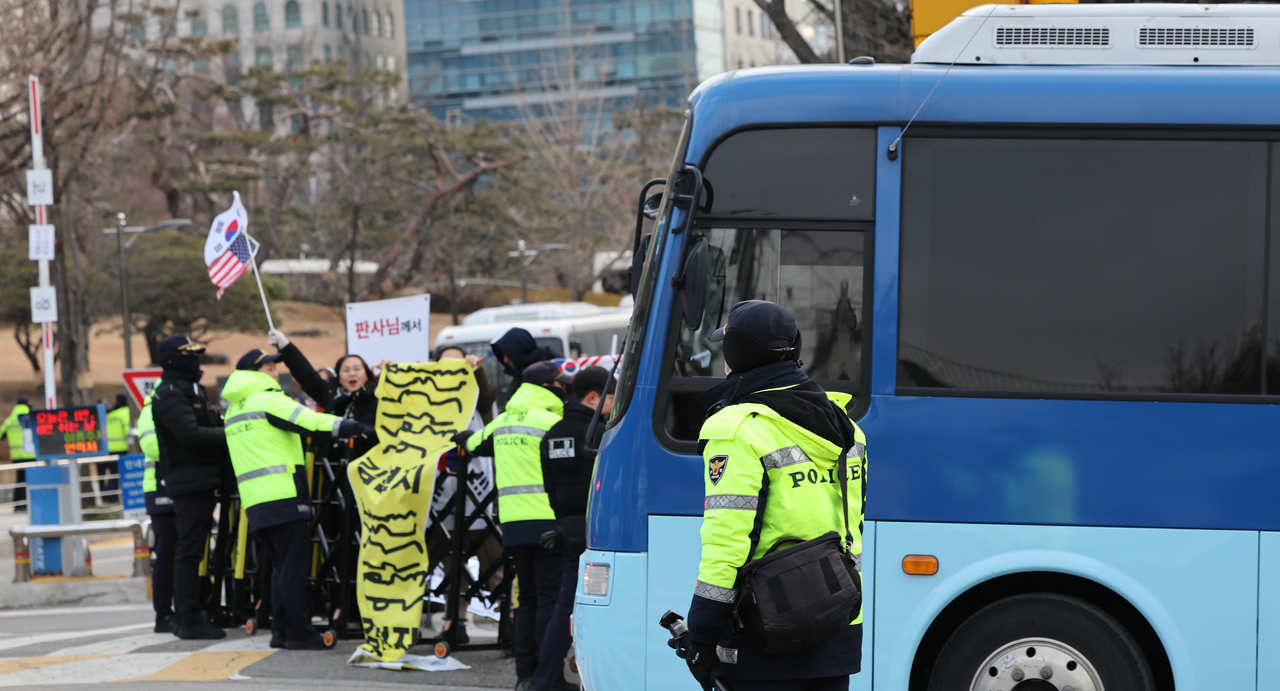 A prisoner transport bus, thought to contain former President Yoon Suk Yeol,  passes by supporters on Monday, as it enters the Seoul Central District Court . (Yonhap)