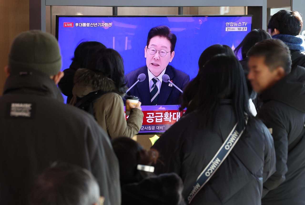 Commuters watch President Lee Jae Myung’s New Year’s press conference broadcast at Seoul Station in Yongsan-gu, Seoul, on Wednesday. (Yonhap)