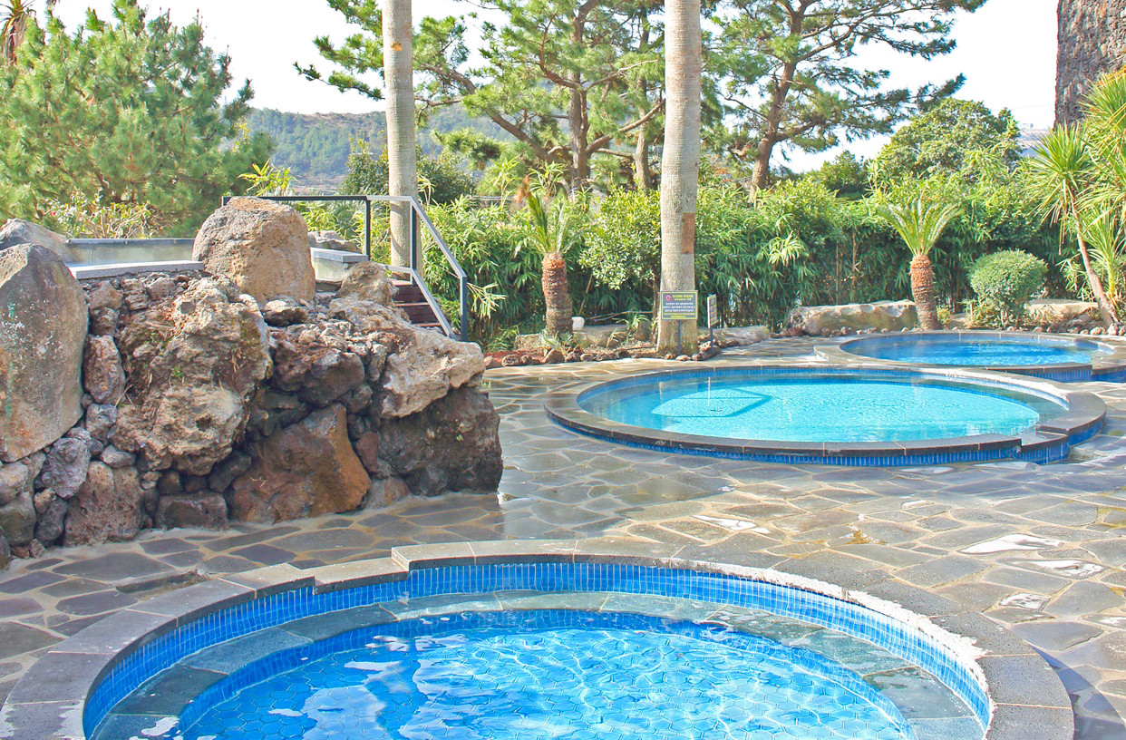 Jeju Sanbangsan Carbonate Hot Springs outdoor bath with volcanic cone visible through glass walls