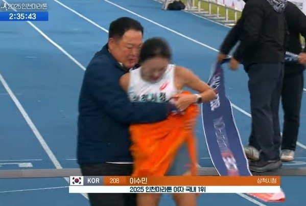 Kim Wan-ki (left), head coach of Samcheok City Hall’s track team, wraps a towel around runner Lee Su-min after she finishes first in the Korean women’s elite full-course race at the 2025 Incheon International Marathon at the Incheon Munhak Sports Complex on Nov. 23. (KBS)