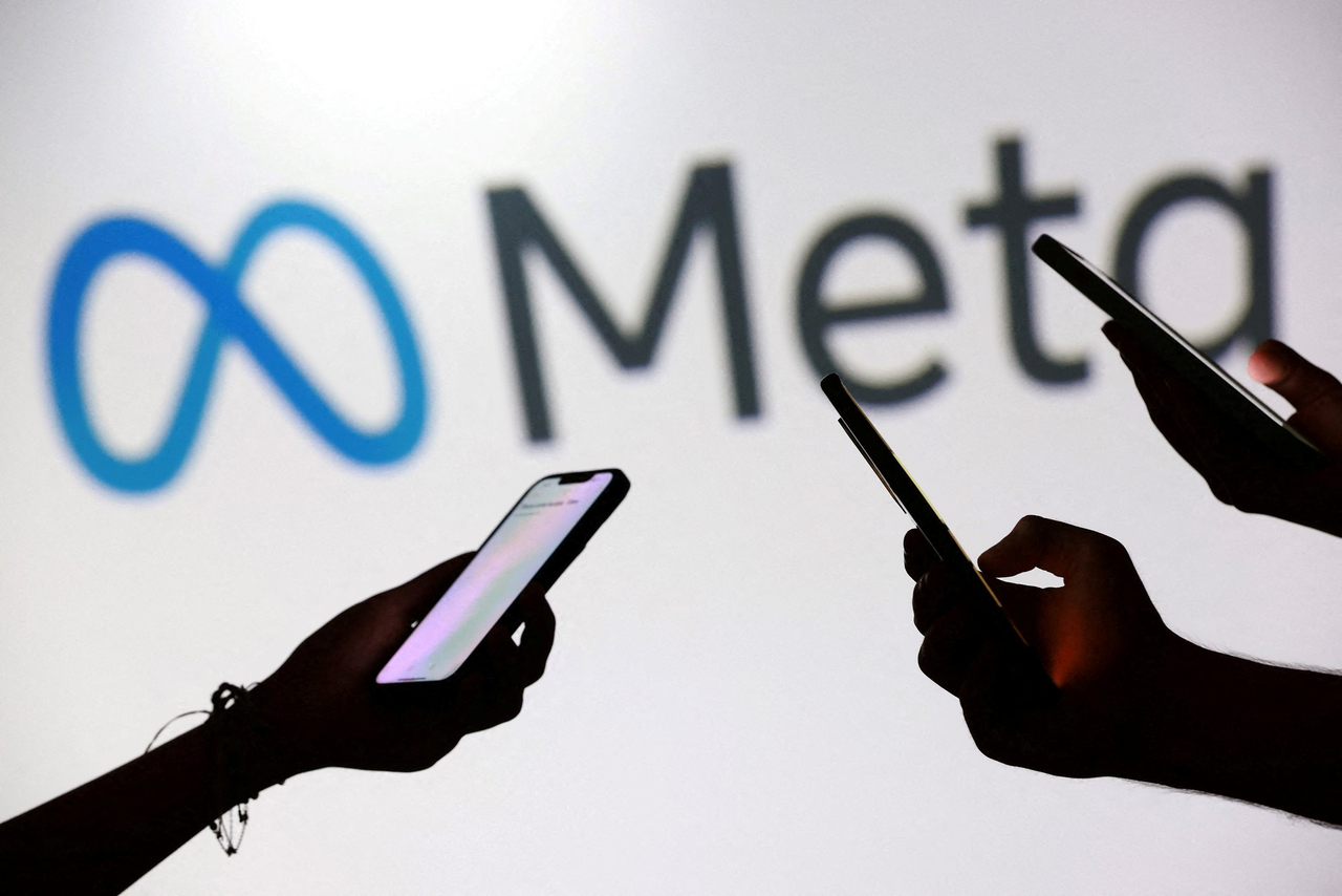 Teenagers pose for a photo while holding smartphones in front of a Meta logo in this illustration.   Reuters-Yonhap