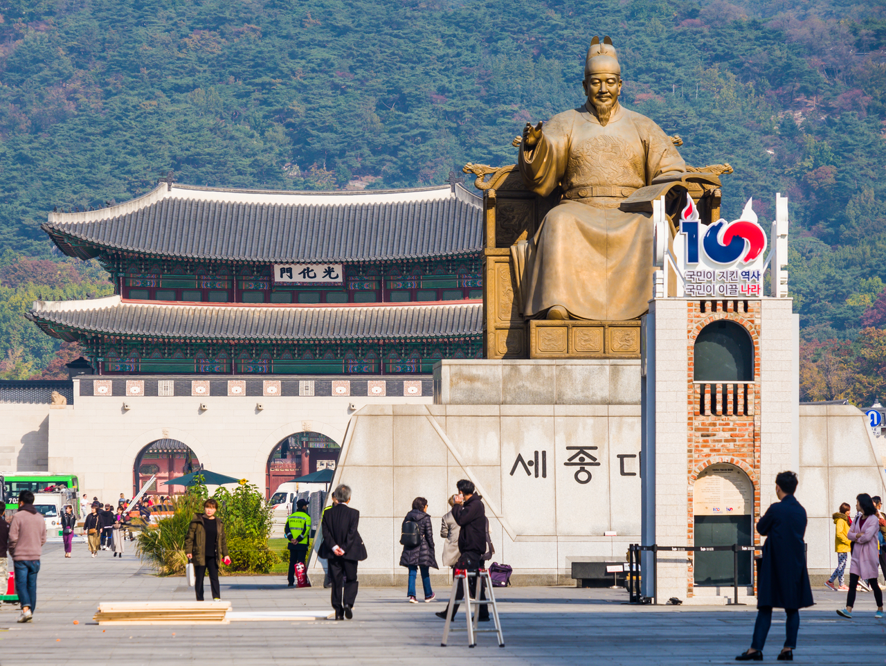 Tourists and locals stroll through the Gwanghwamun Plaza, overlooked by the statue of King Sejong and the green slopes of Bukhansan beyond (Getty Image)