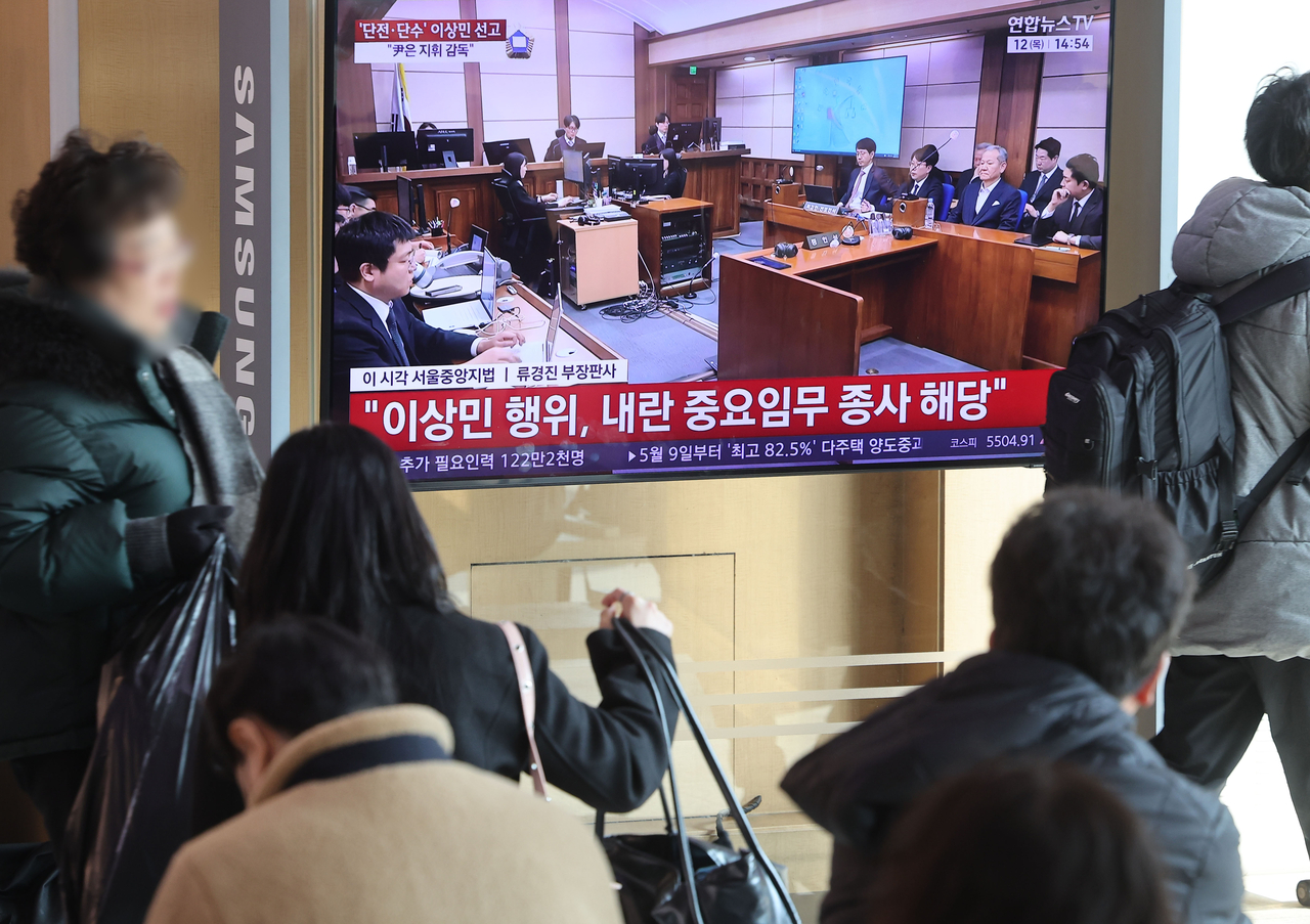 Commuters watch former Interior Minister Lee Sang-min's sentencing on TV at Seoul Station on Thursday. (Yonhap)