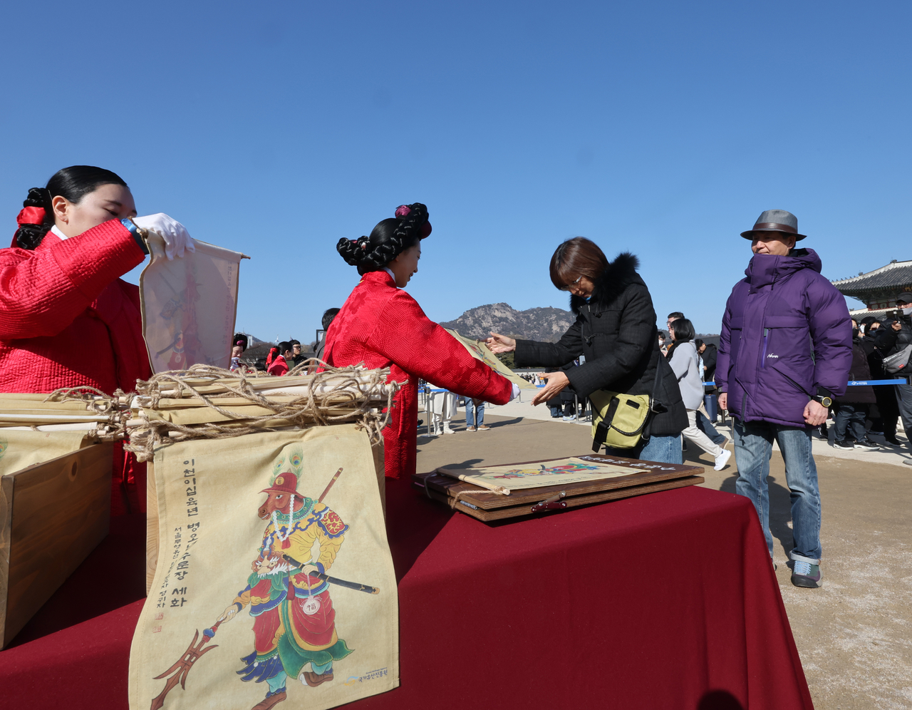 Visitors receive traditional New Year paintings at the “2026 Byeong-o Year Sehwa Sharing” event held at Heungnyemun Square of Gyeongbokgung Palace in Seou on Monday, a day before the Lunar New Year holiday. (Yonhap)