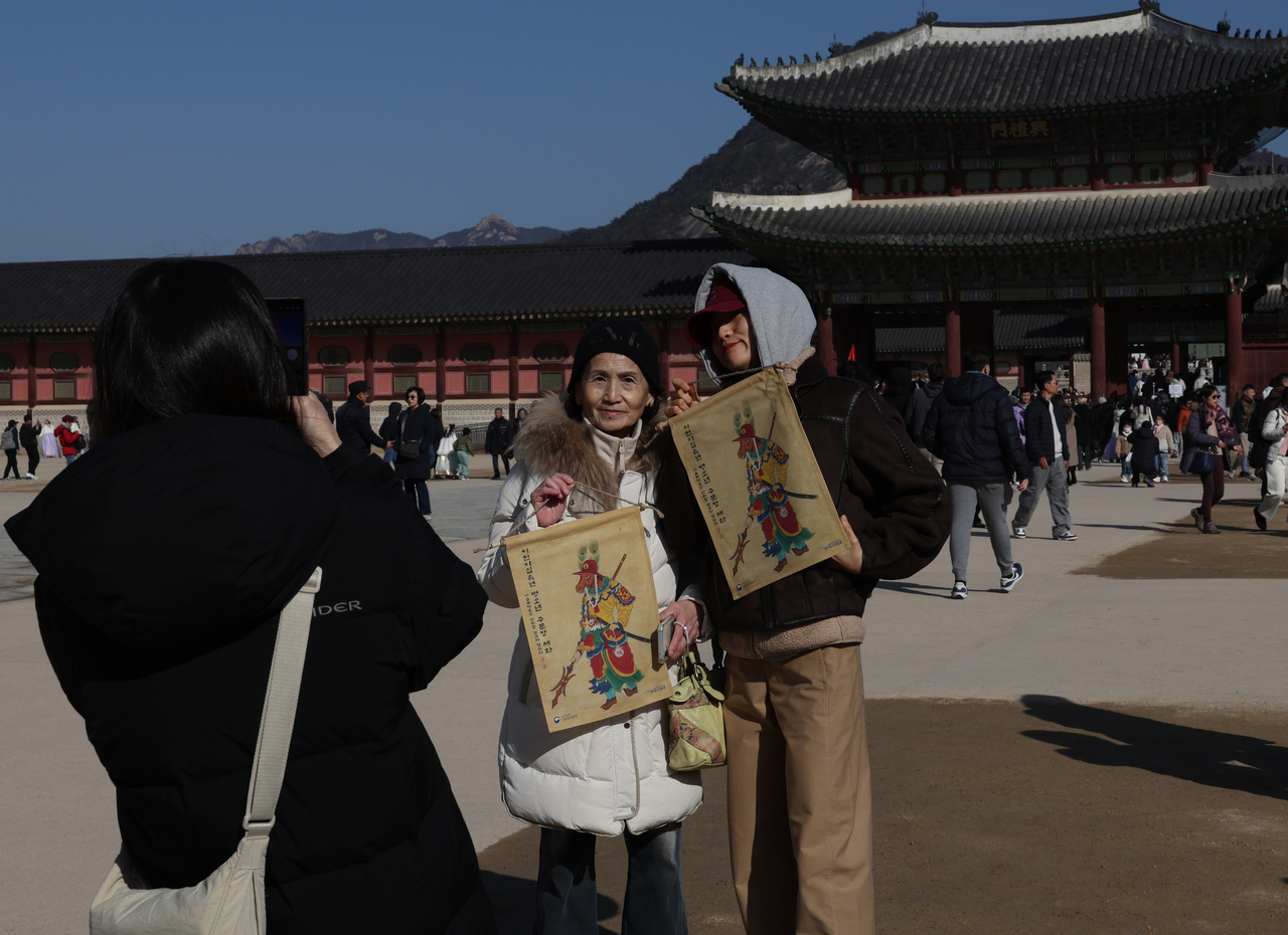 Visitors pose for a commemorative photo while holding traditional New Year paintings at the “2026 Byeong-o Year Sehwa Sharing” event held at Heungnyemun Square of Gyeongbokgung Palace in Seoul on Monday, a day before the Lunar New Year holiday. (Yonhap)