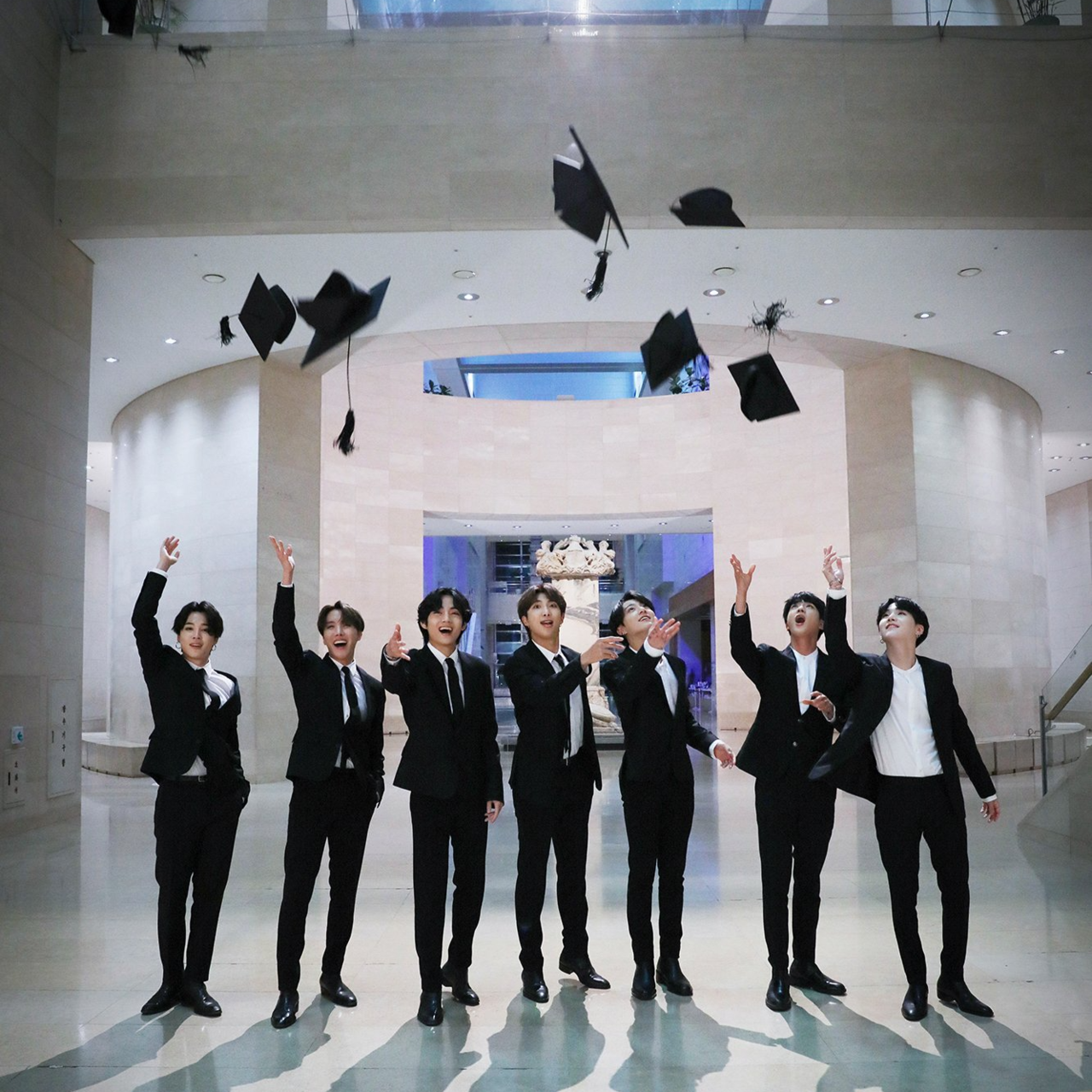 The BTS members throw graduation caps into the air at the National Museum of Korea for YouTube's 