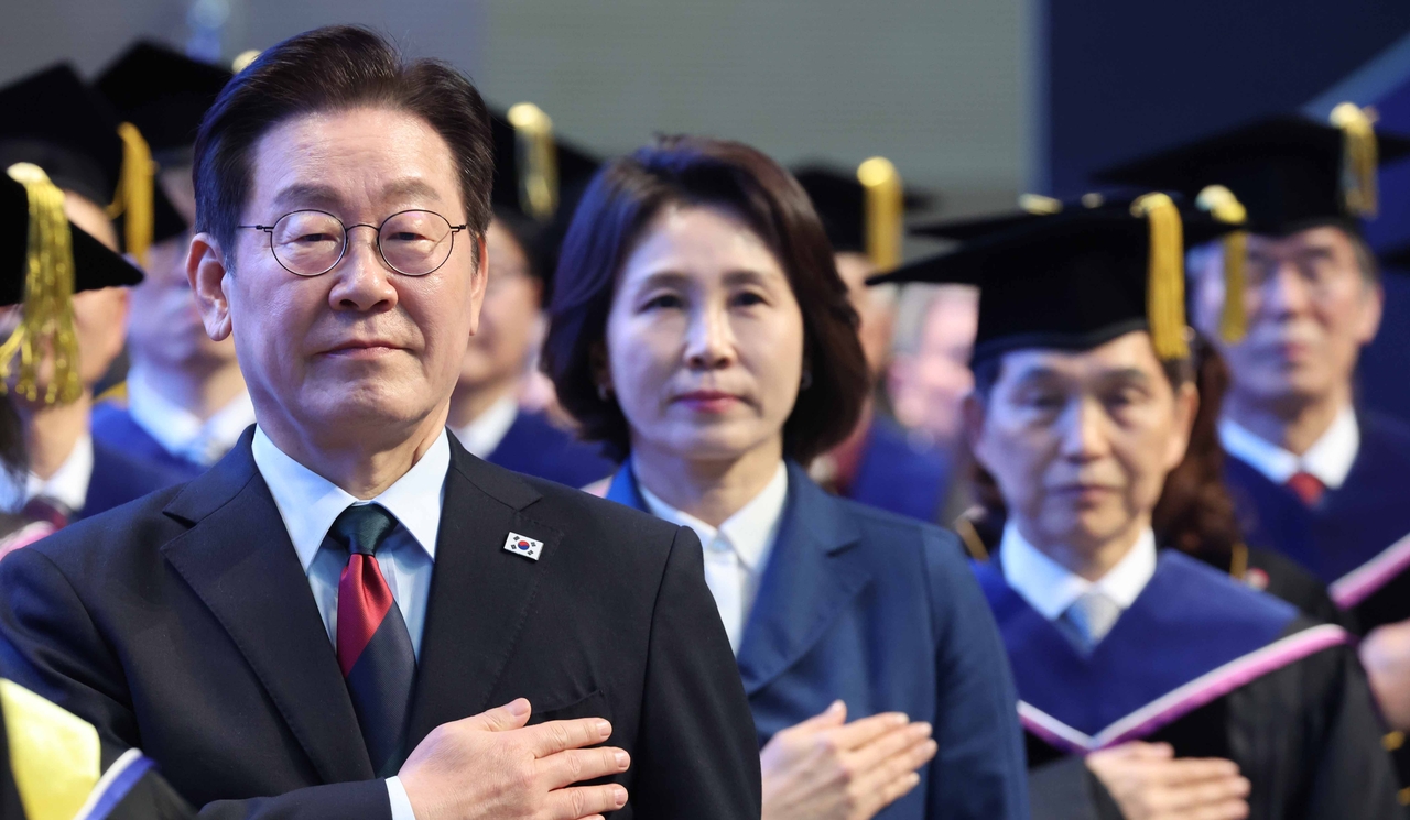 President Lee Jae Myung (left) and his wife Kim Hea Kyung (second from left) salute the national flag at a commencement ceremony for the Korea Advanced Institute of Science and Technology in Daejeon on Friday. (Yonhap)