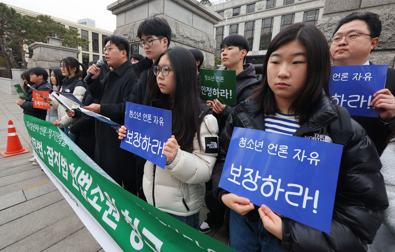 Student journalists from Tokipul, including Moon Sung-ho (front, third from right), hold up signs during a press conference on Tuesday in front of the Constitutional Court, before submitting their constitutional complaint. (Yonhap)