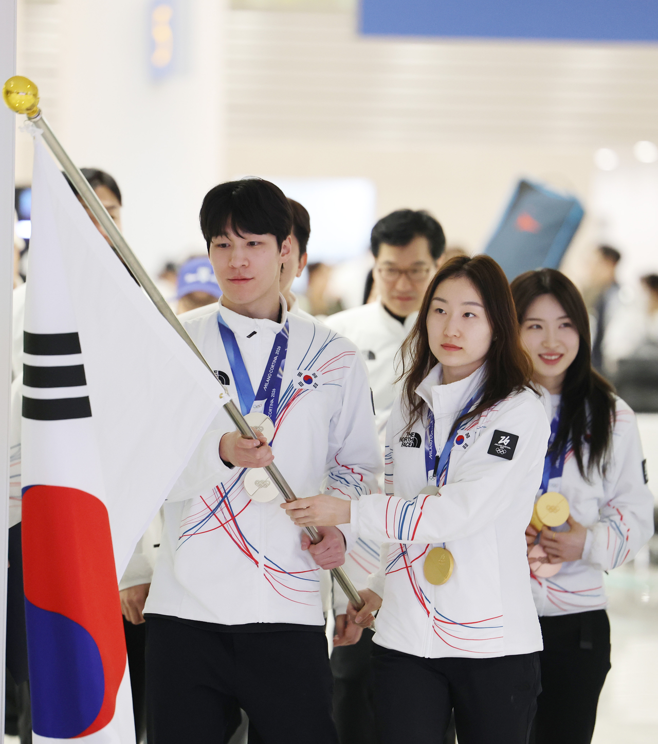 South Korean short track speed skaters Hwang Dae-heon (left) and Choi Min-jeong (center) carry the national flag, Taegeukgi, to lead the way for the South Korean delegation at Incheon International Airport, west of Seoul, upon its return from the Milan-Cortina Winter Olympics on Tuesday. (Yonhap)