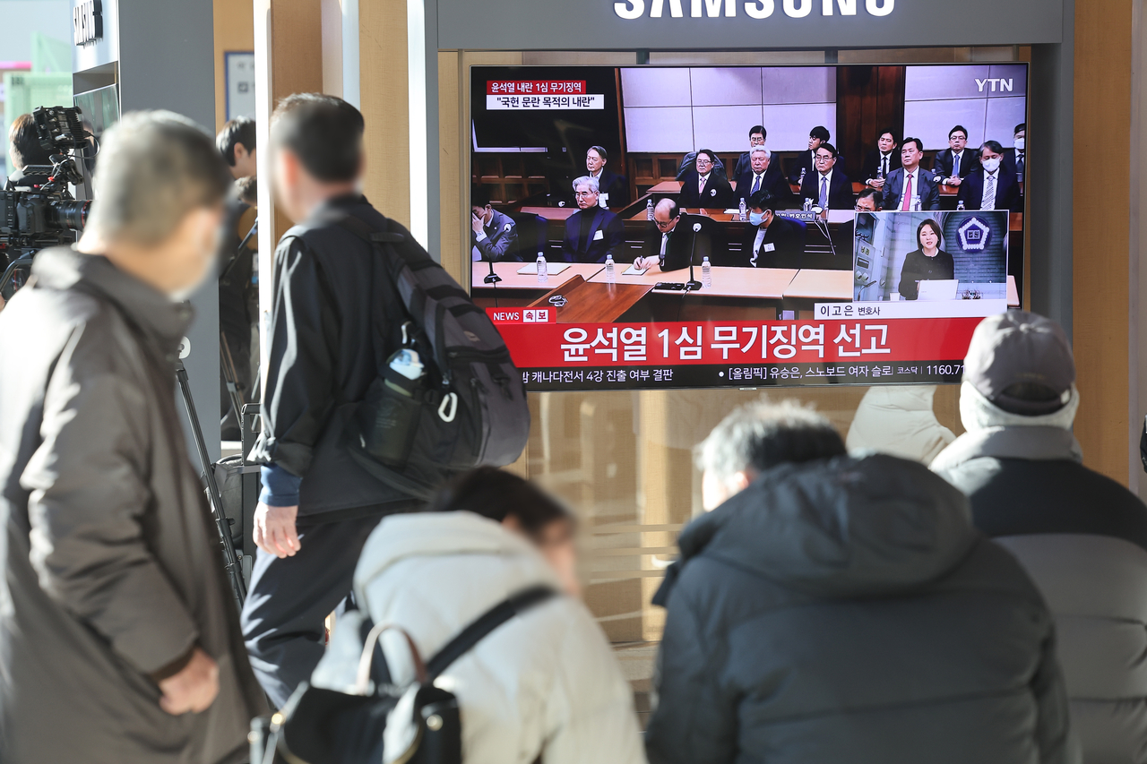 People watch a live TV broadcast at Seoul Station in the capital on Feb. 19, 2026, that shows jailed former President Yoon Suk Yeol attending a court hearing to receive the first verdict on whether his 2024 imposition of martial law constituted an insurrection following special prosecutors' recommendation of the death penalty. The court convicted Yoon of leading an insurrection through his failed martial law imposition. (Yonhap)