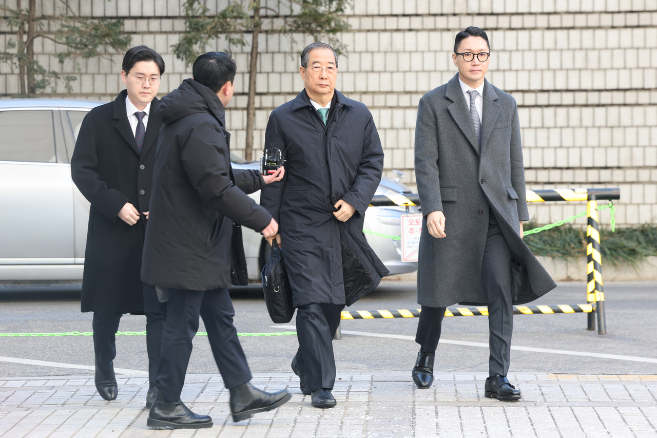 Former Prime Minister Han Duck-soo (second from right) is approached by a reporter as he walks to the Seoul Central District Court on Jan. 21, ahead of his sentencing for playing a key role in insurrection. (Yonhap)