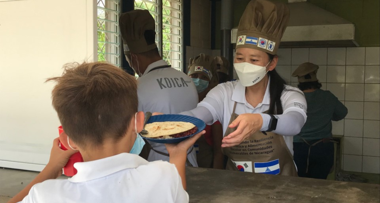 This photo shows a senior official of the state-runn Korea International Cooperation Agency serving a school meal to a child in El Madrono Elementary School in Jinotega, Nicaragua, in May 2022. (Korea International Cooperation Agency)
