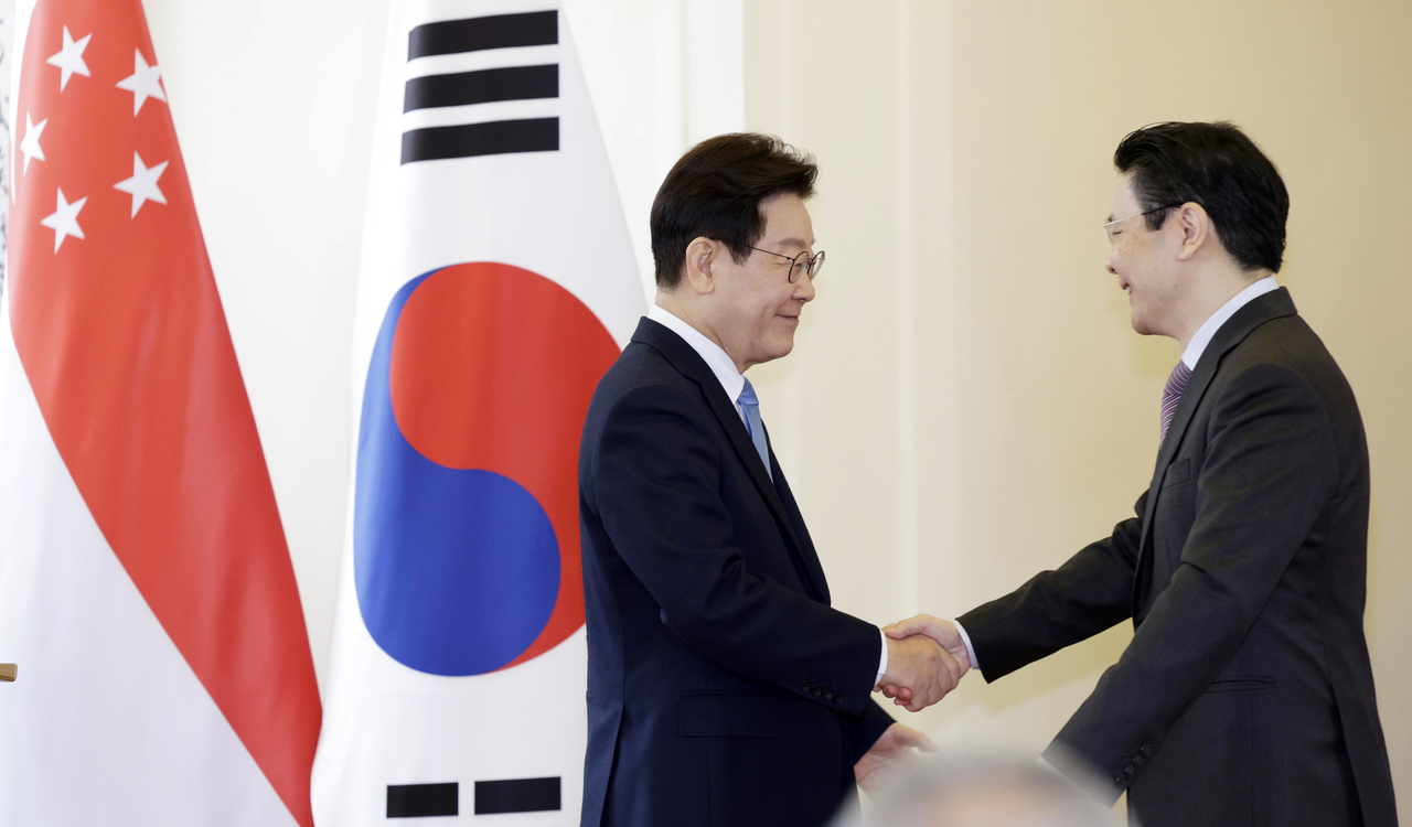 President Lee Jae Myung (left) shakes hands with Singaporean Prime Minister Lawrence Wong in Singapore on Monday. (Yonhap)
