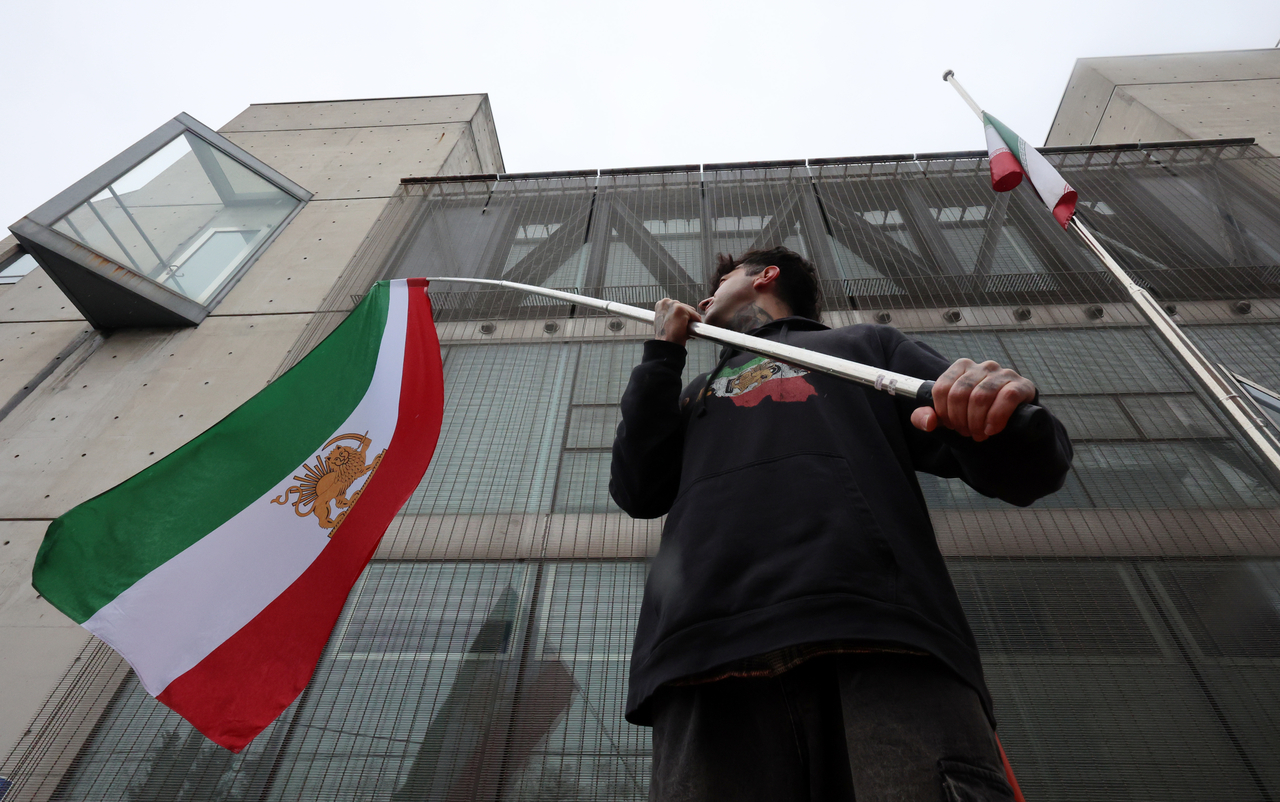An Iranian waves former Persian flag in front of the Embassy of the Islamic Republic of Iran in Yongsan-gu, Seoul, Saturday. On the right, the embassy's official flag of Iran is flown at half-staff to commemorate the death of Supreme Leader Ali Khamenei. (Newsis)