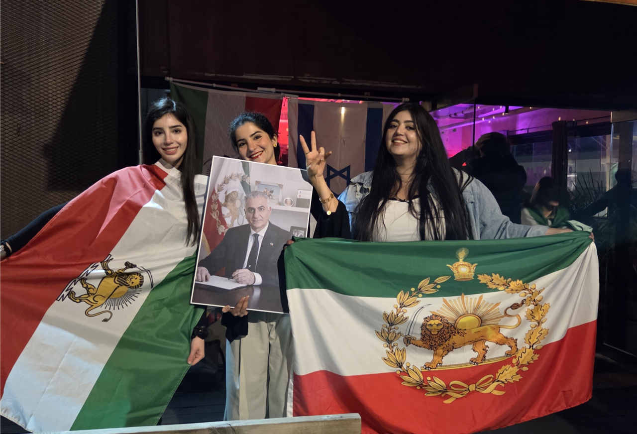 Iranians in Seoul, including Niusha (first rom left), Sanaz (second from left) and Kiana (third from left) hold up the former Persian flag and a portrait of Iran's last crown prince, Reza Pahlavi, during a party held on Sunday in Seongdong-gu, Seoul. (Sanaz)
