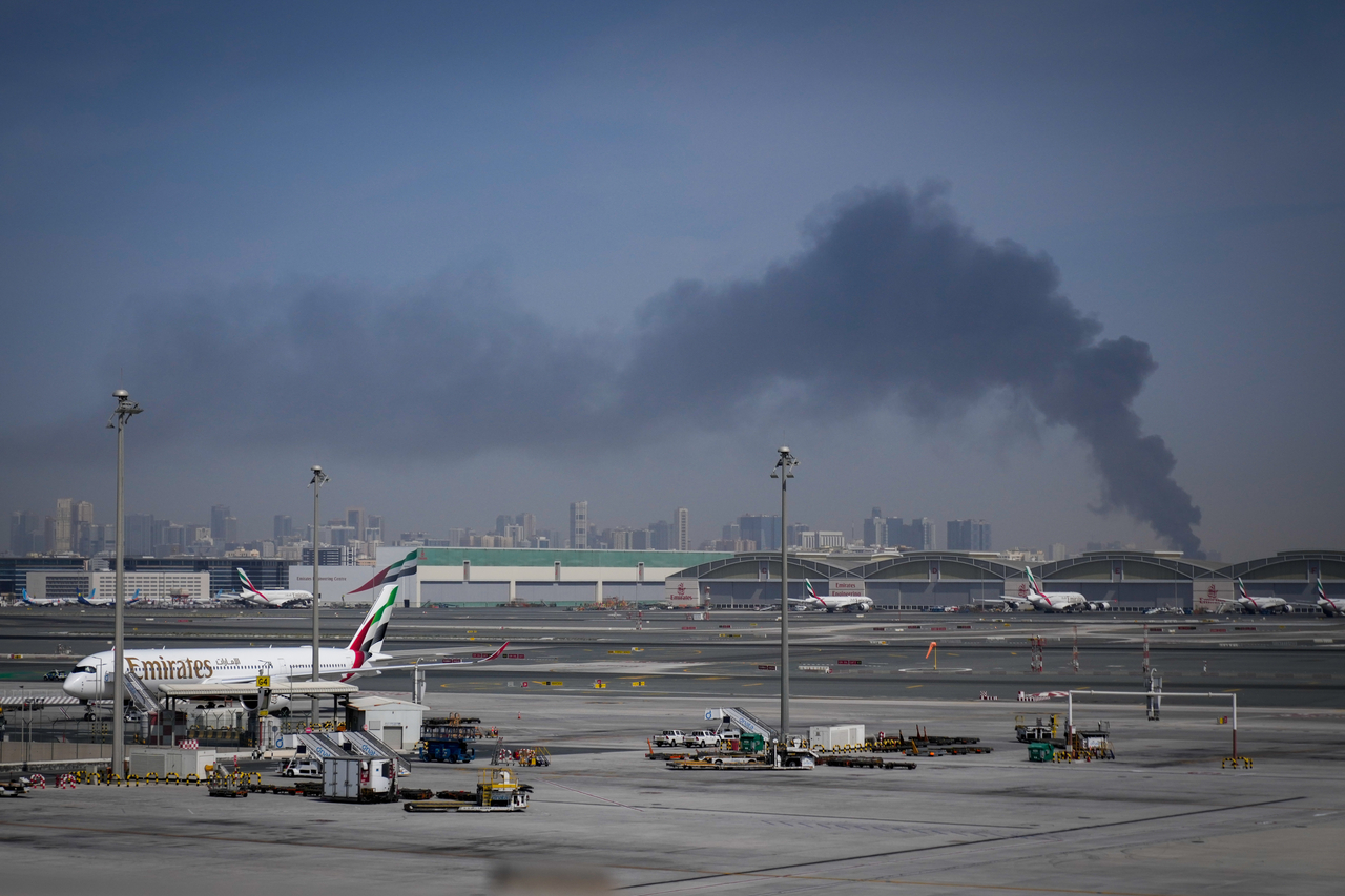 A plume of smoke caused by an Iranian strike is seen in the background as Emirates planes are parked at Dubai International Airport after its closure in Dubai, United Arab Emirates on March 1, 2026. (AP-Yonhap)