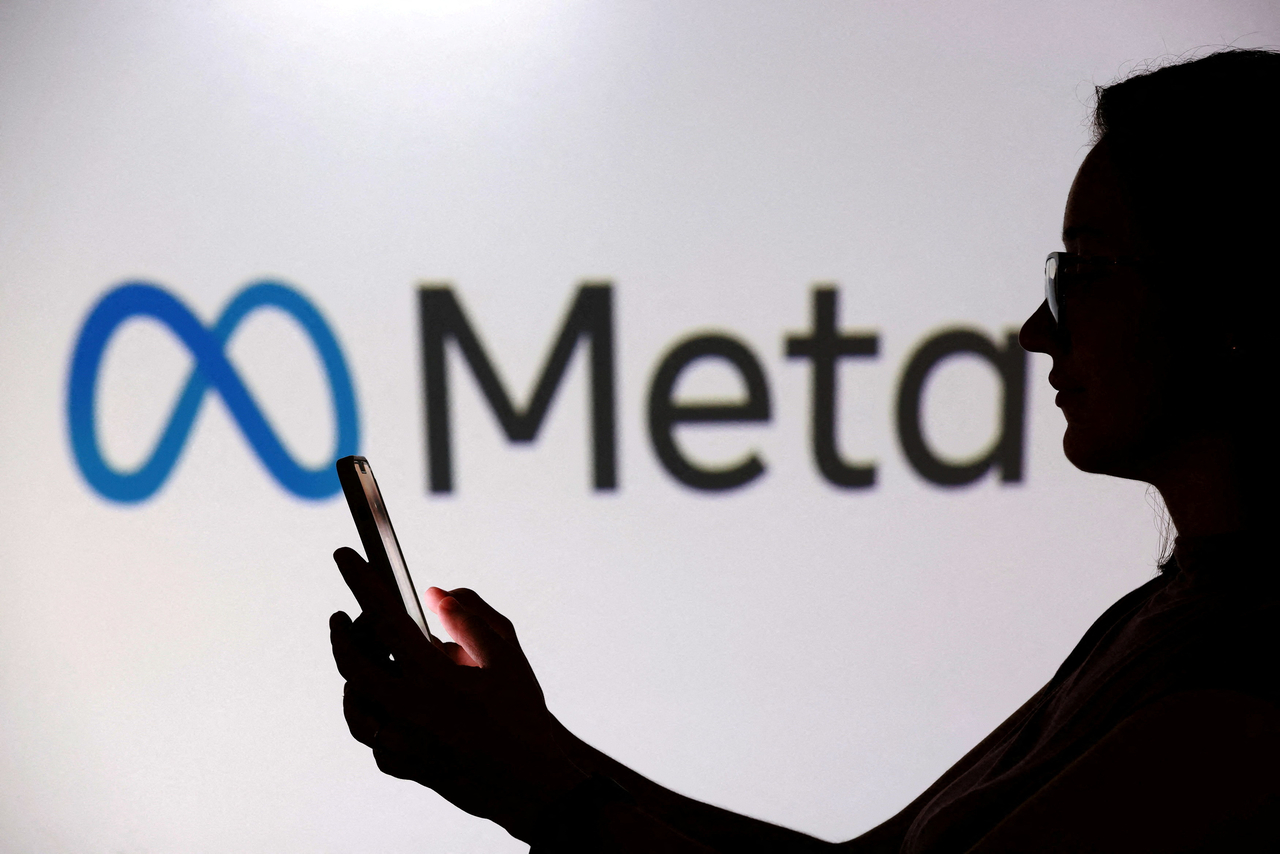 A teenager poses for a photo while holding a smartphone in front of a Meta logo.   Reuters-Yonhap