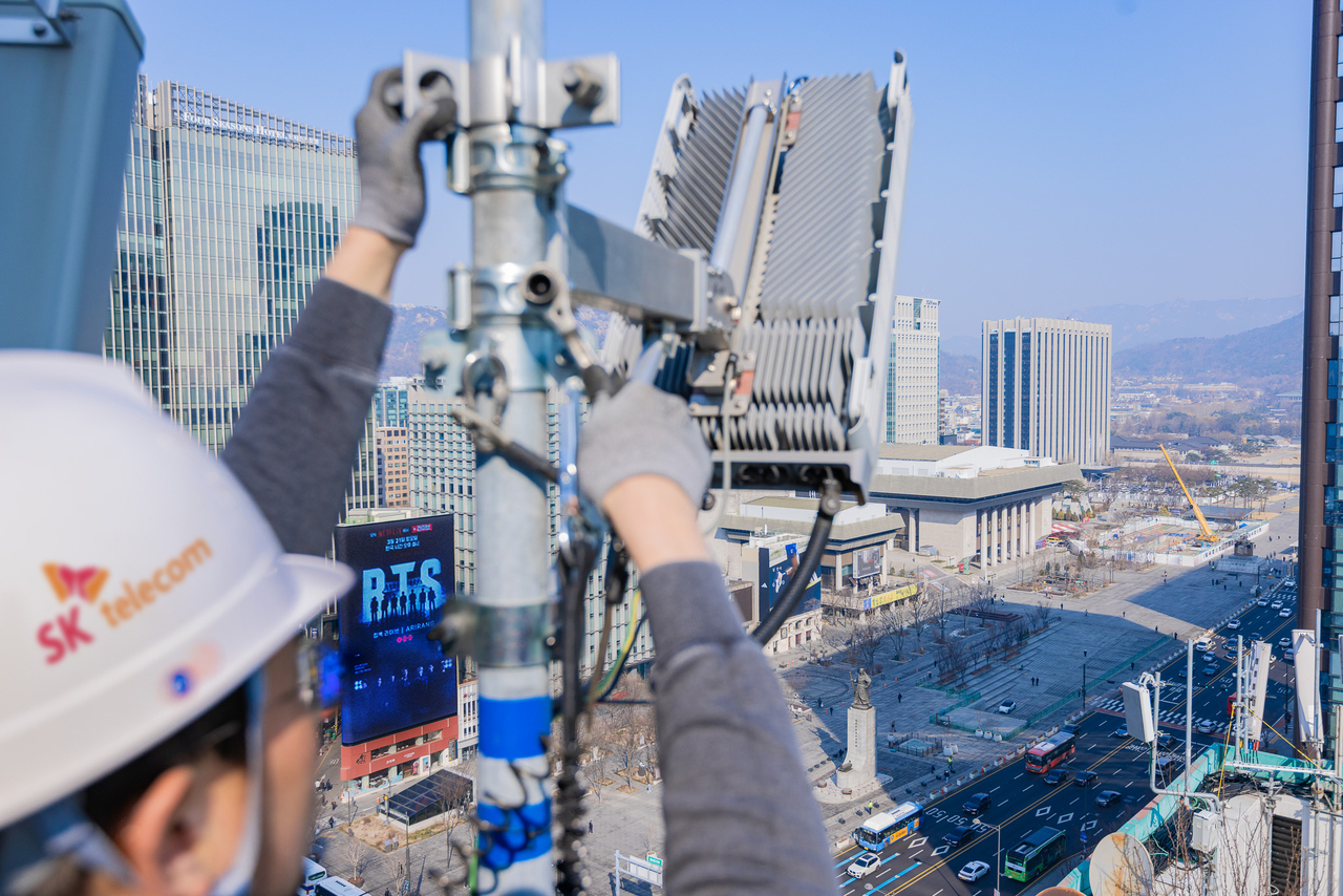 An SK Telecom engineer inspects a base station antenna overlooking Gwanghwamun Square, where a BTS concert promotional display is visible on a nearby building. (SK Telecom)