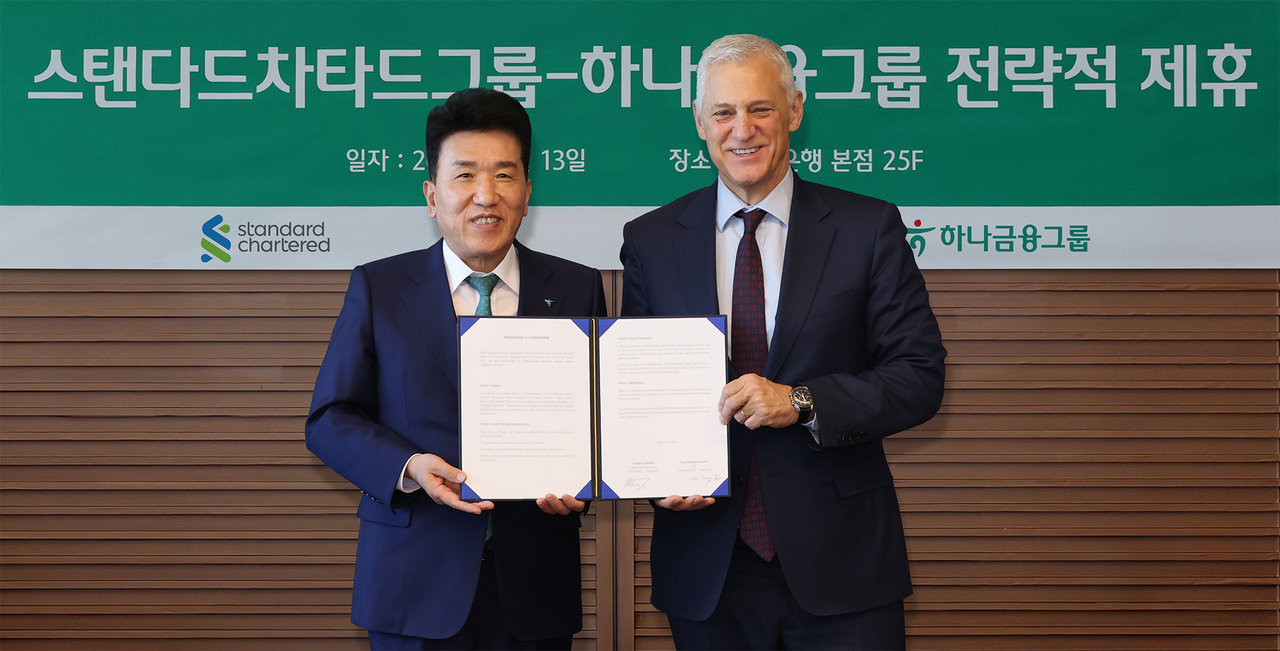 Hana Financial Group Chairman Ham Young-joo (left) and Standard Chartered Group CEO Bill Winters pose for a photo while holding the agreement after signing a memorandum of understanding on cooperation in global business and digital assets at Hana Bank’s headquarters in central Seoul. (Hana Financial Group)