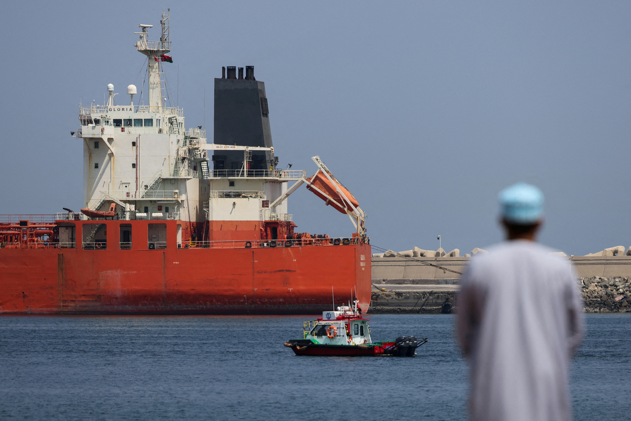 A man stands near the waterfront as a vessel sits at anchor, amid the US-Israeli conflict with Iran, at Sultan Qaboos Port in Muscat, Oman, Monday.   Reuters-Yonhap