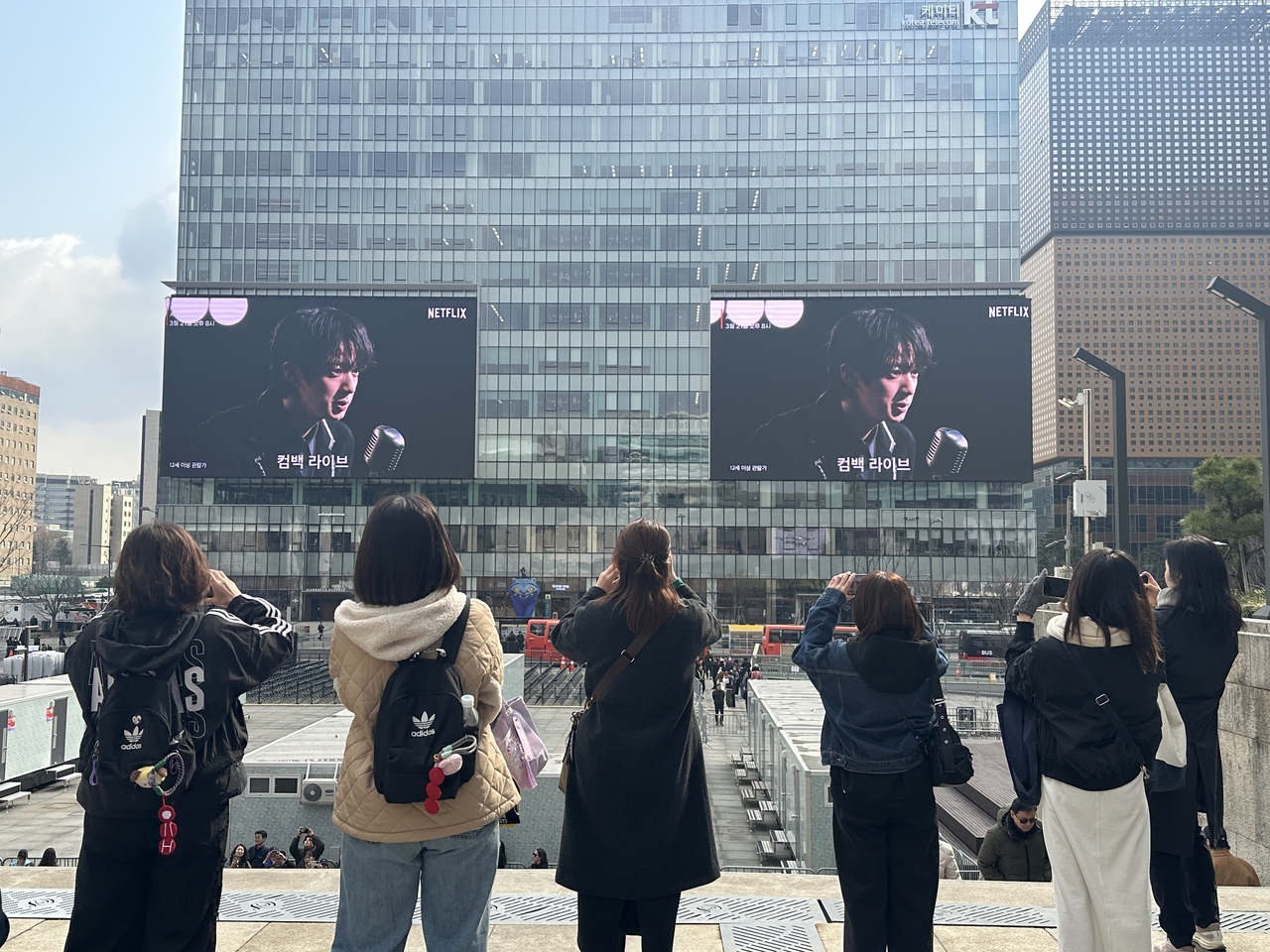 Fans take a photo of Netflix's advertisement for BTS' comeback show at Gwanghwamun Square playing on the megascreens of KT Gwanghwamun Building West on Friday. (Lee Jung-joo/The Korea Herald)