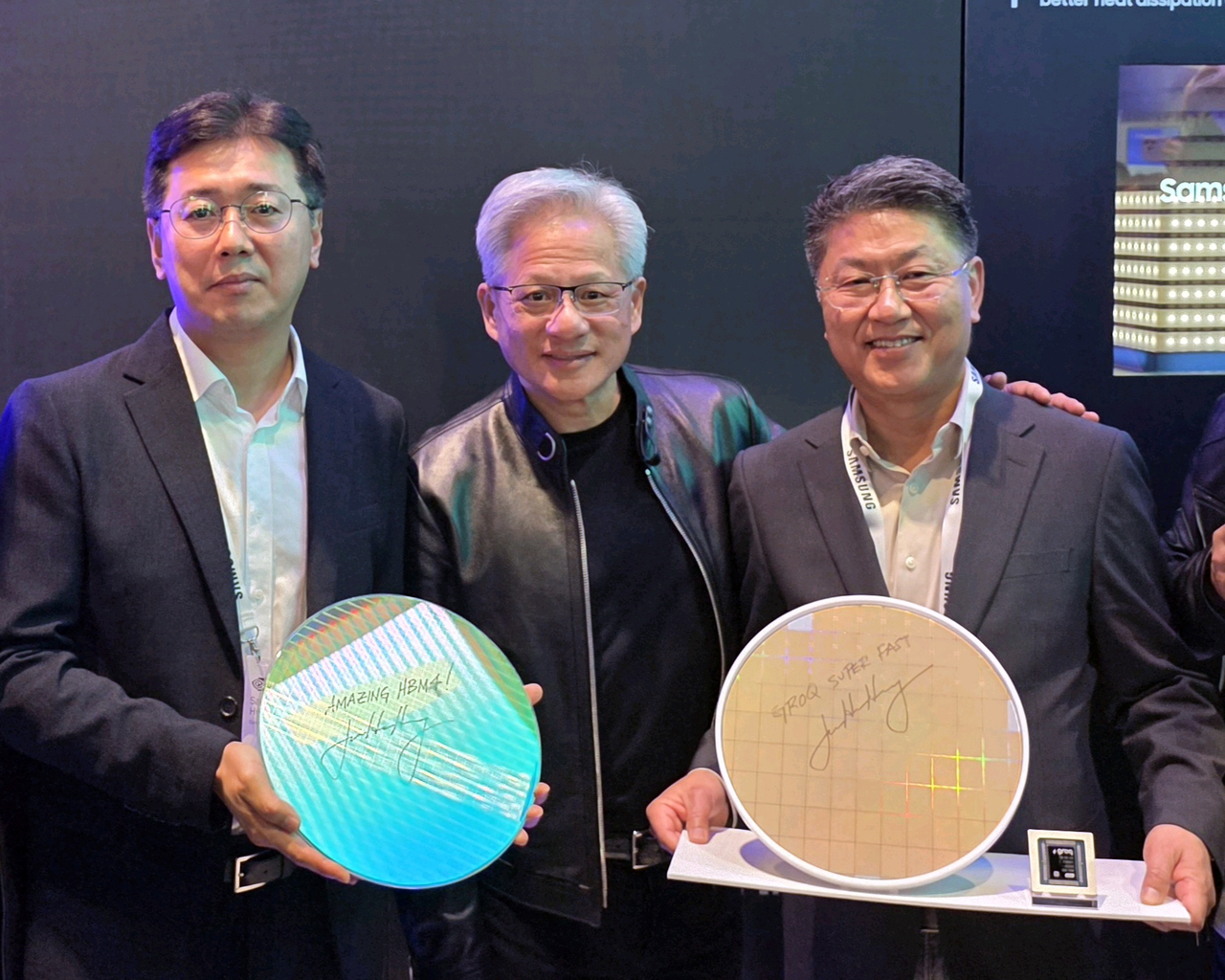 Jensen Huang, CEO of Nvidia, poses with Samsung Electronics executives Hwang Sang-joon (left), vice president of memory development, and Han Jin-man, president and head of the foundry business, at Samsung’s booth during GTC 2026 in San Jose on Monday. The executives are holding a Samsung HBM4 core-die wafer and a 4-nanometer Groq LPU foundry wafer, both signed by Huang.
(Samsung Electronics)
