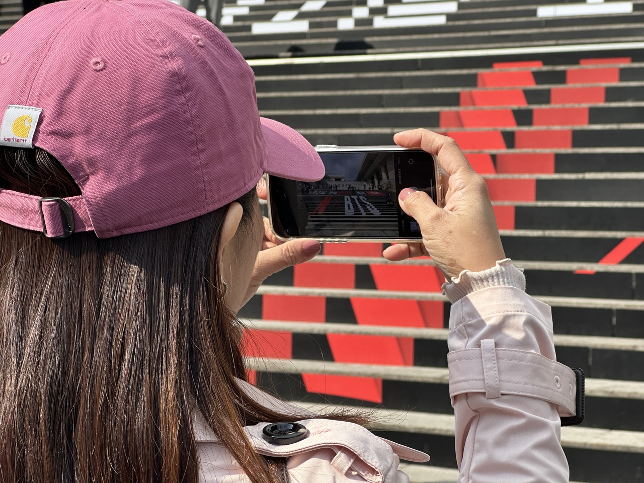 A fan is seen taking a photo of the stairs by the Sejong Center for the Performing Arts where promotional material for BTS' full-group comeback concert is displayed, Friday. (Lee Jung-joo/The Korea Herald)