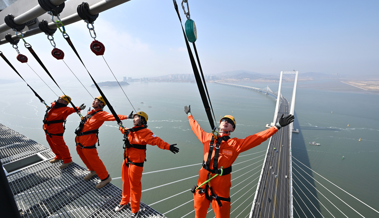 People teeter on the rim of the observatory facility of Incheon Cheongna Sky Bridge linking Yeongjongdo, the island home to Incheon International Airport, with the mainland, in Incheon, west of Seoul, on March 25, 2026, as they experience an "edge walk" attraction, where visitors can stroll in an open-air space overlooking the Yellow Sea, ahead of its opening next month. The observatory has been recognized by Guinness World Records and the US-based World Record Committee as the world's highest observatory on a sea bridge. (Yonhap)