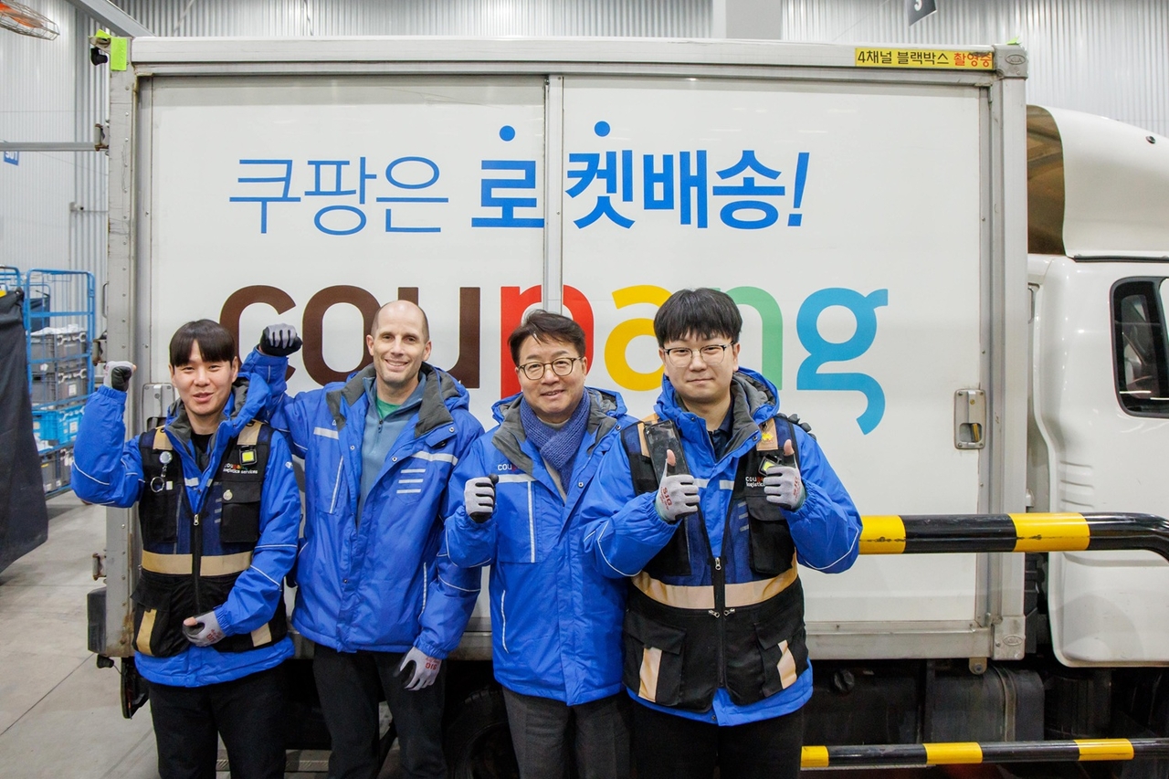 Coupang interim CEO Harold Rogers (second from left) and Rep. Yeom Tae-young (third from left) pose for a photo with Coupang delivery workers at a Coupang logistics service center in Seongnam, Gyeonggi Province, March 19. (Coupang)