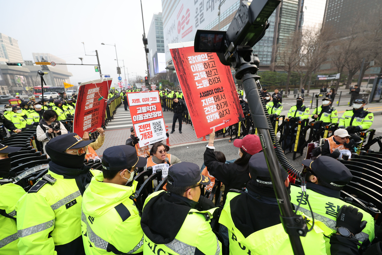 Police on Friday blockade Saejong-daero and surround activists as they stage a guerilla boarding protest at a nearby bus stop. (Yonhap)