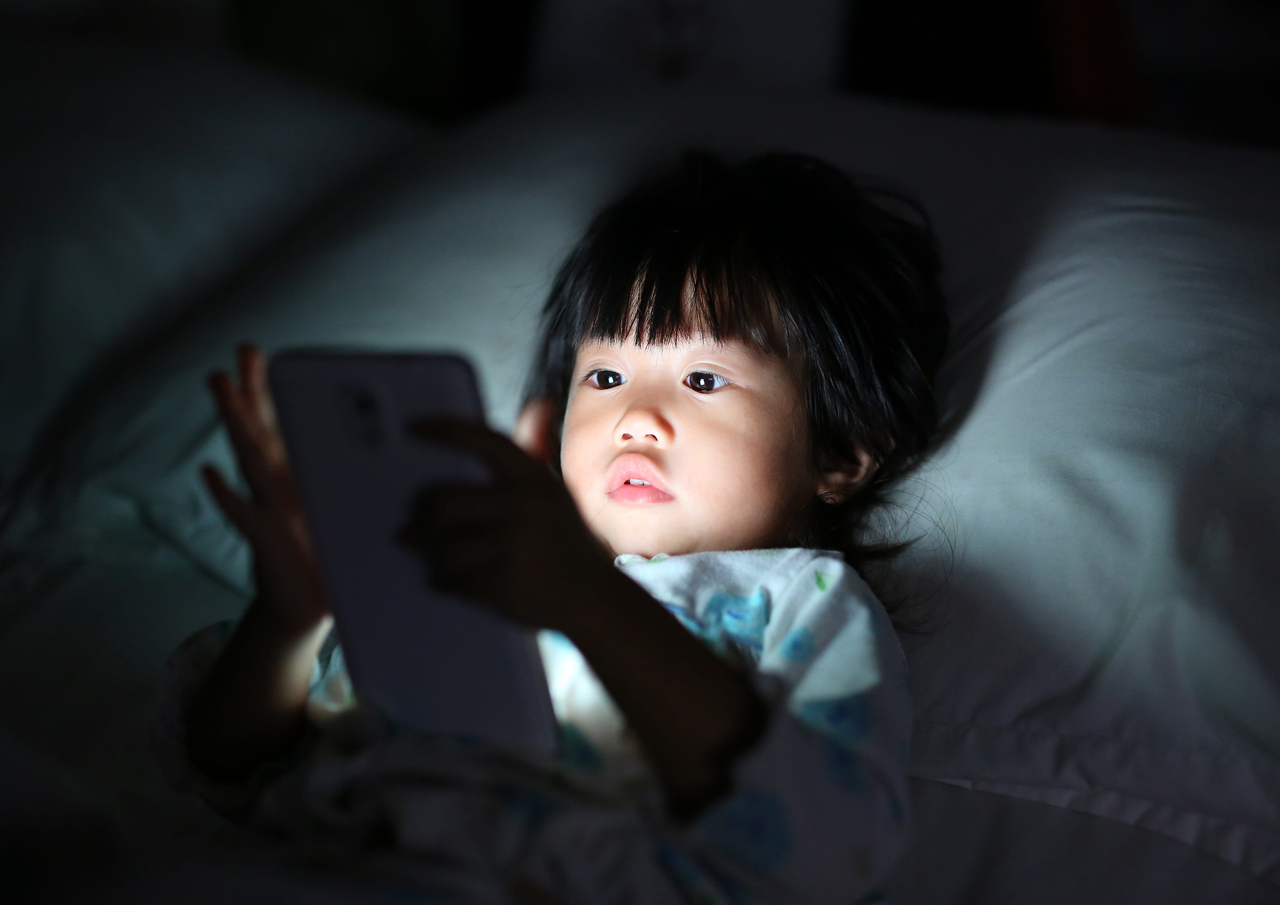 A girl plays smartphone lying on a bed. (123rf)