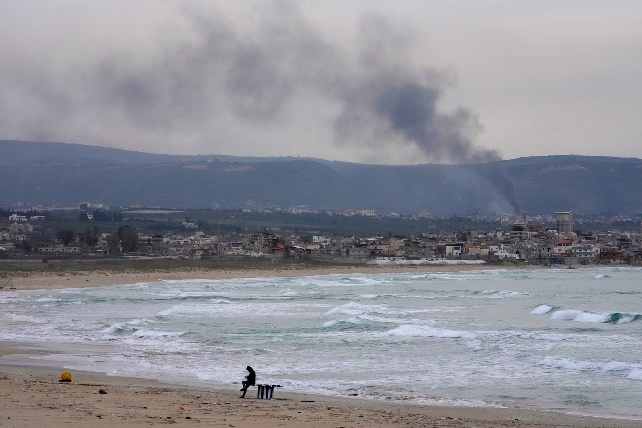 A man checks his mobile phone on a public beach, as smoke, background, rises from Israeli artillery shells on Qlaileh village, as it s seen from Tyre city, south Lebanon, Saturday. (AP-Yonhap)