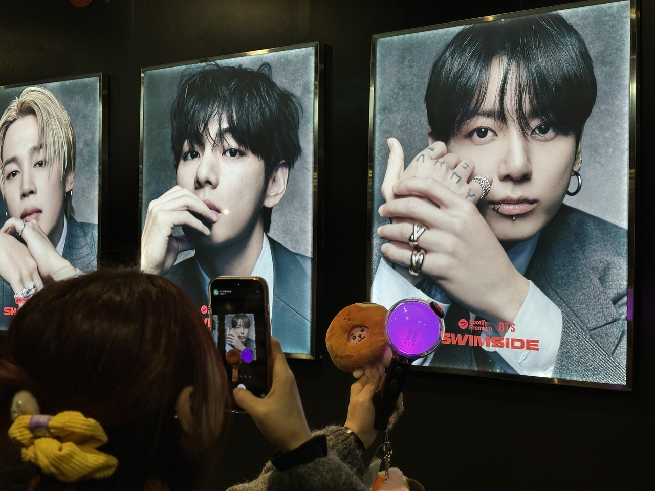 A BTS fan poses with her Army Bomb and Cooky plushie in front of Jungkook's photo on the Spotify X BTS Swimside cruise in Seoul.