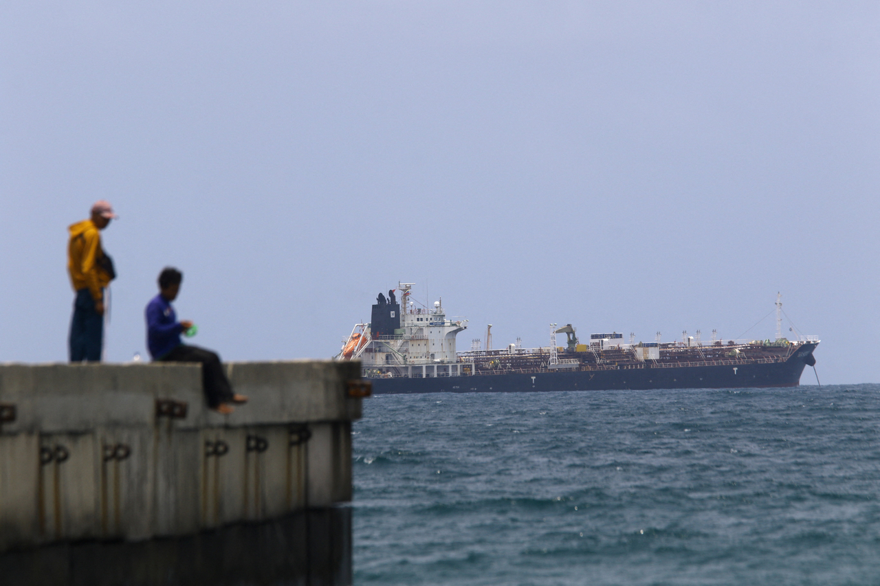 People sit on a dock as the Hong Kong-flagged vessel Sea Horse, carrying Russia-origin fuel originally bound for Cuba, is anchored near the coast of Puerto Cabello, Venezuela, Saturday. (Reuters-Yonhap)