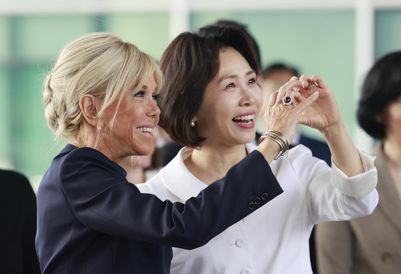 Korean first lady Kim Hea Kyung (right) and French first lady Brigitte Macron make finger hearts for visitors at the National Museum of Korea in Seoul on Friday. (Pool photo via Yonhap)
